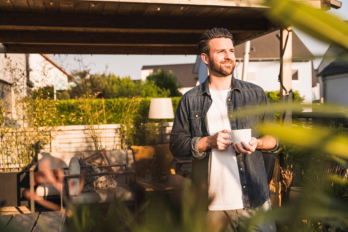 Individual standing outdoors on a patio holding a coffee mug