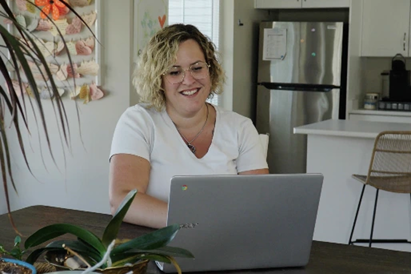 a woman sitting at her kitchen table on her laptop