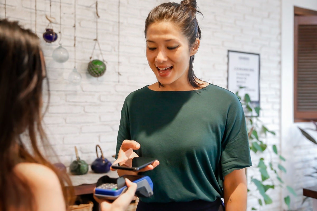 Customer paying with a smartphone while a shop staff member holds a card reader in a retail setting.