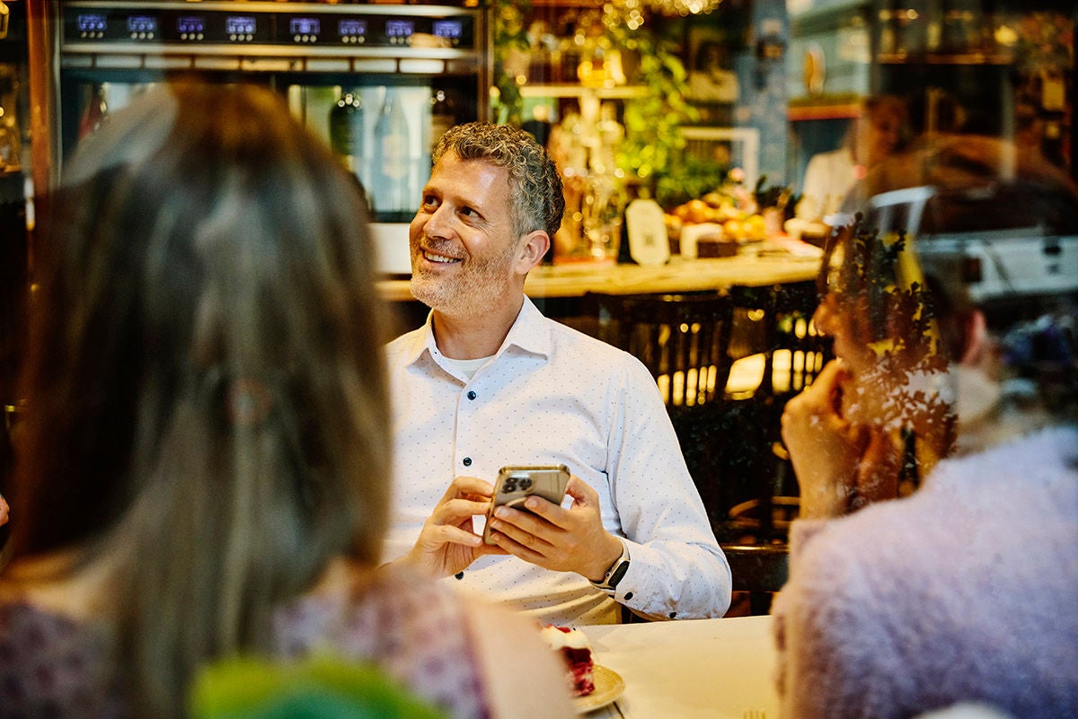 Person holding a smartphone at a café table, sitting together with business partners