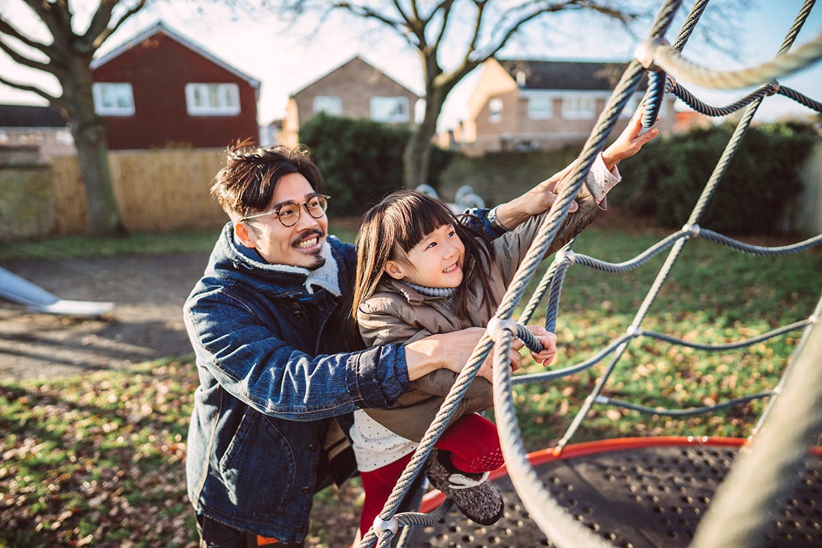 Lovely little girl plying on the climbing web with her young handsome dad in play park joyfully.