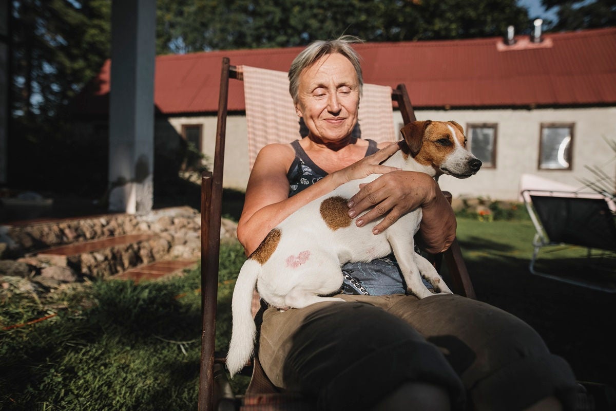 A person relaxes in a lawn chair outdoors, holding a small dog on their lap in the warm afternoon sun.