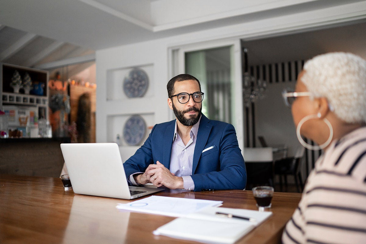 Two people sit at a table in a modern home setting, having a professional conversation.