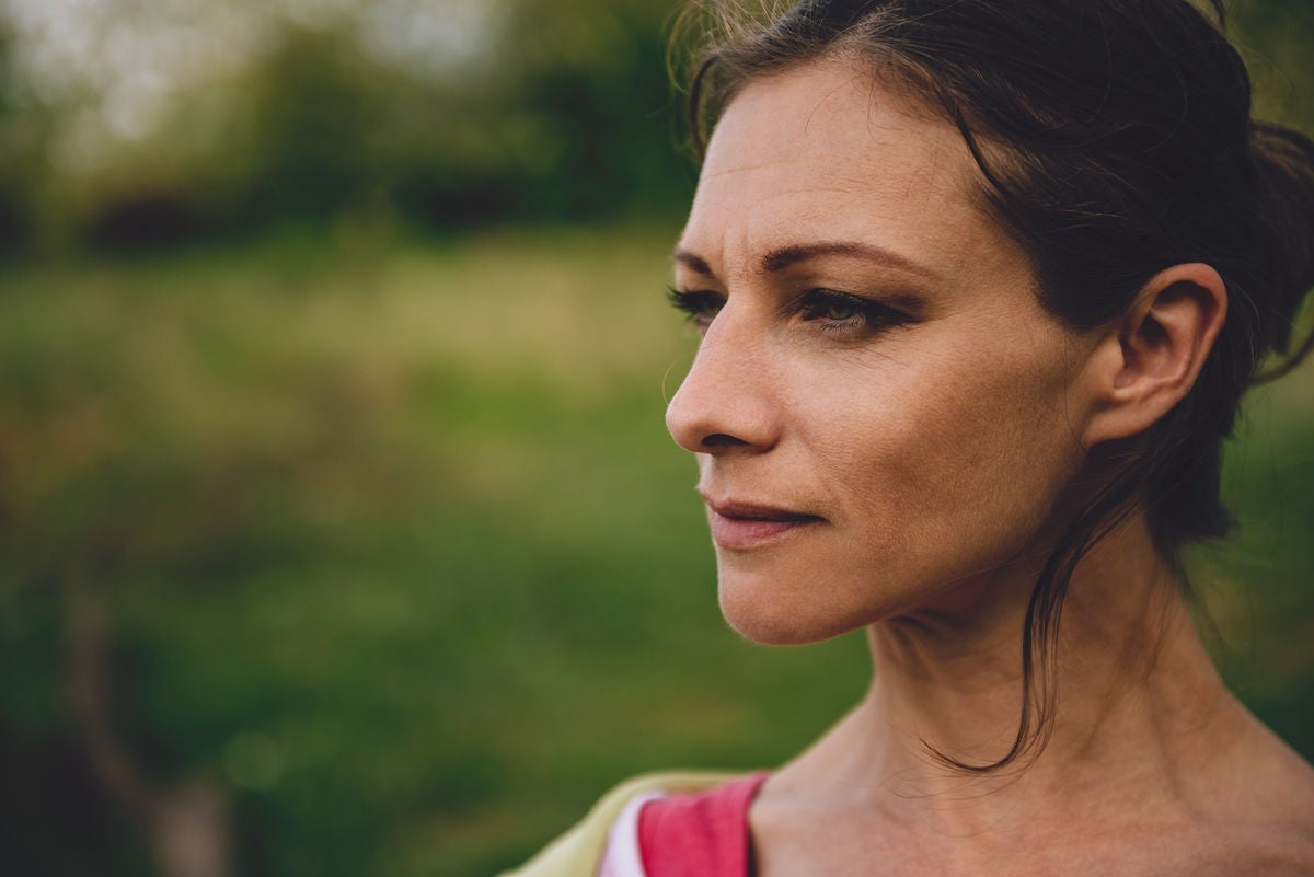 A determined young woman standing outdoors in a natural, green setting.