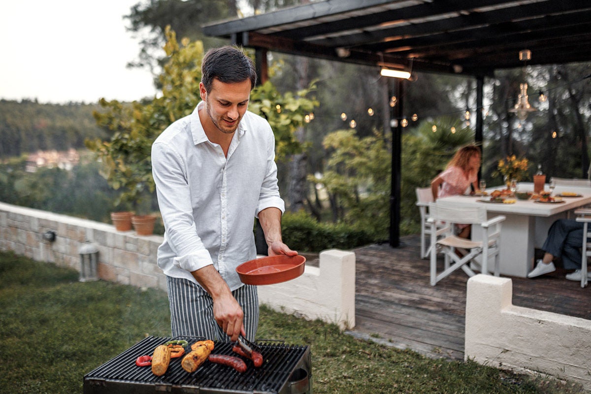 Handsome young man making barbeque for dinner party at his back yard
