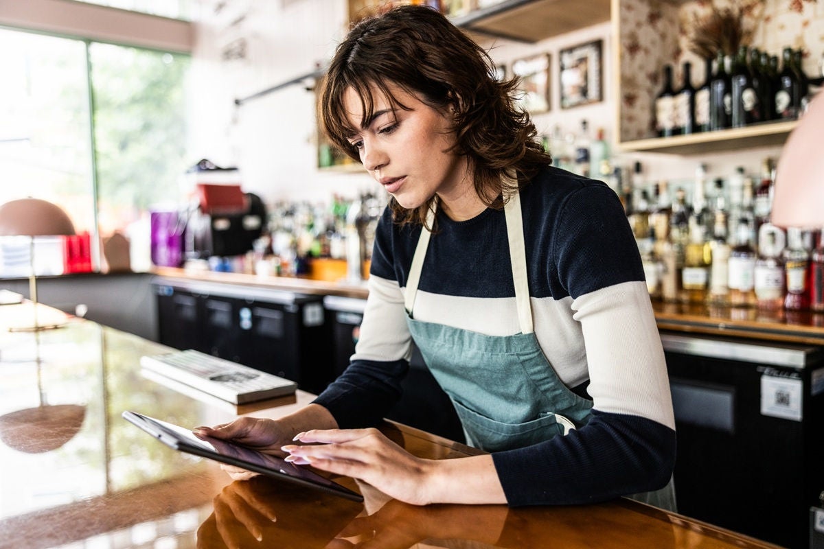 Cafe owner using a tablet to manage orders and use online banking at the counter.
