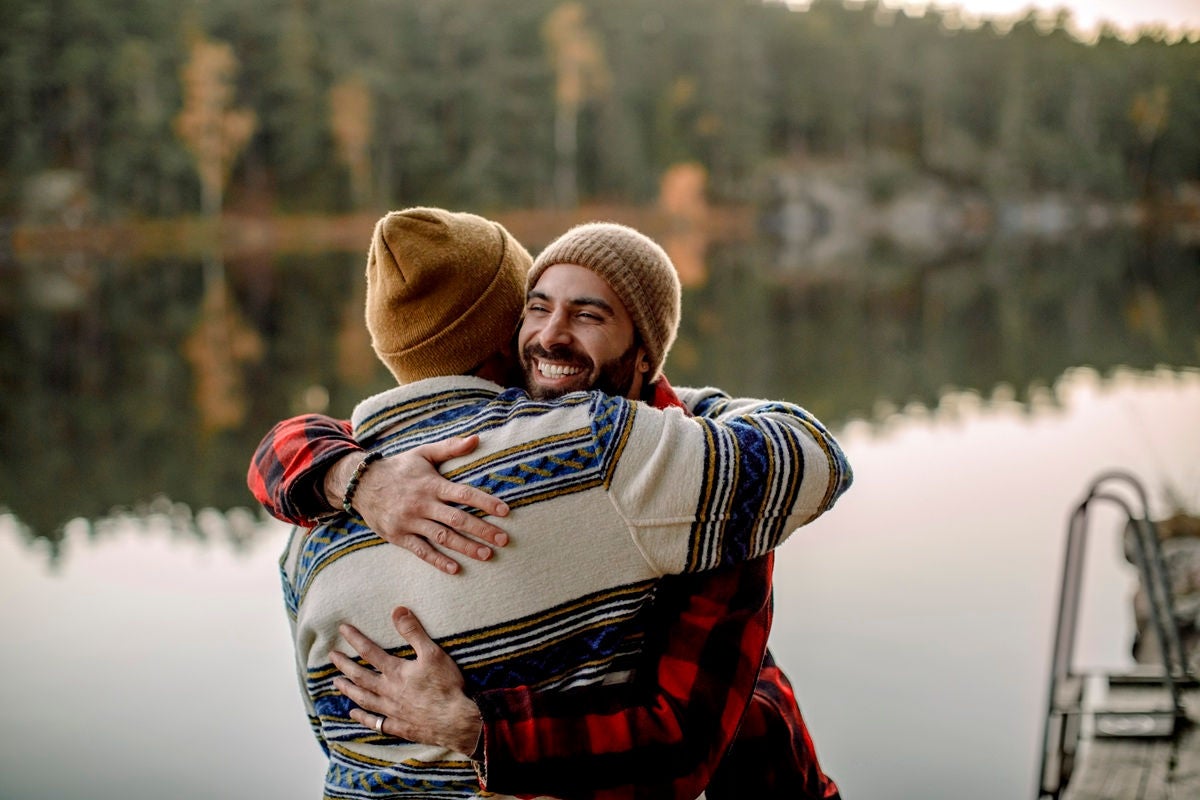 Two people sharing a warm hug by a lakeside.