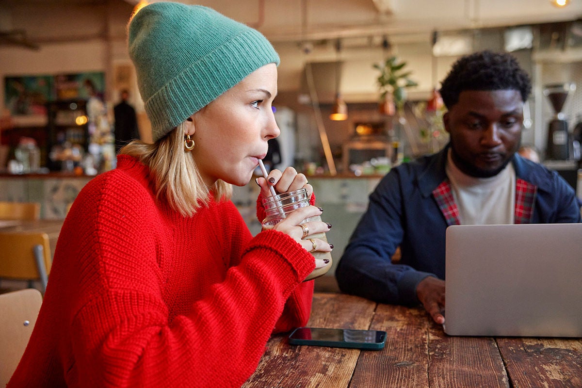 A a young woman taking a break while her friend works on his laptop - hybrid workspace