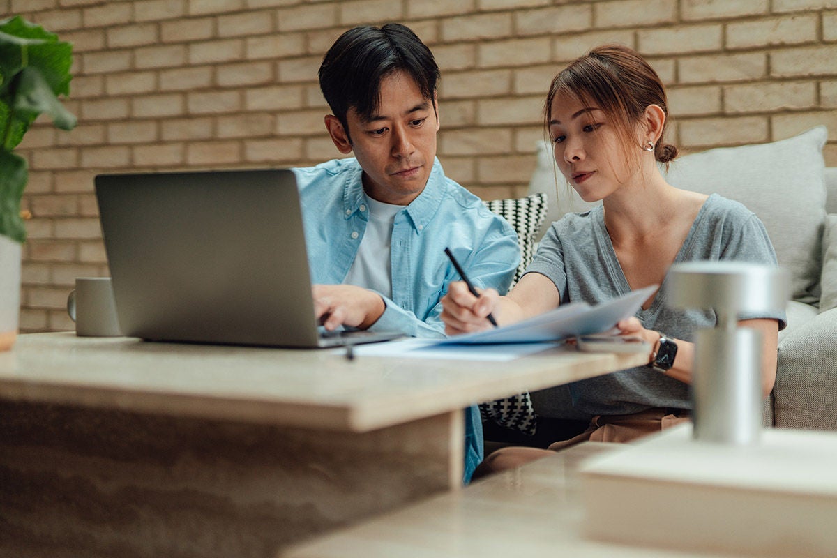 Two people sitting at a table reviewing financial documents together while working on a laptop