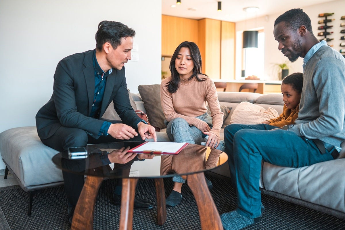 A professional meeting with a family seated in a living room, reviewing documents on a coffee table.
