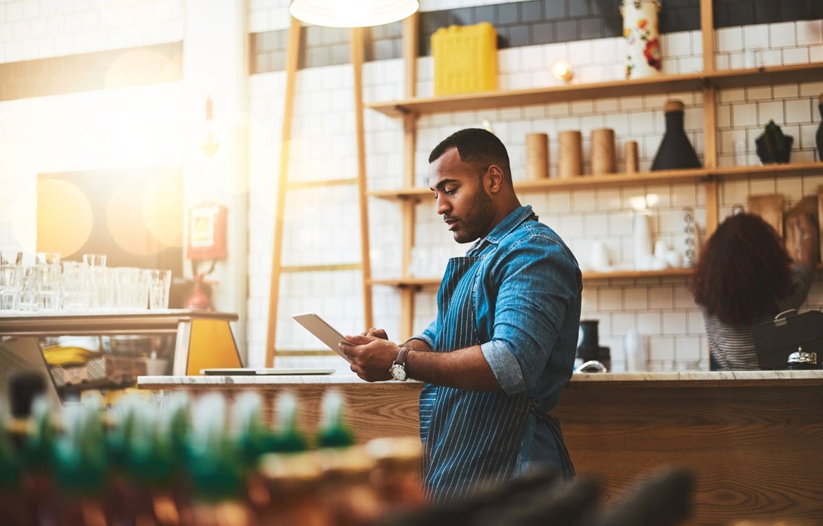 Small business owner reviewing invoices and payment information behind the counter of a café.