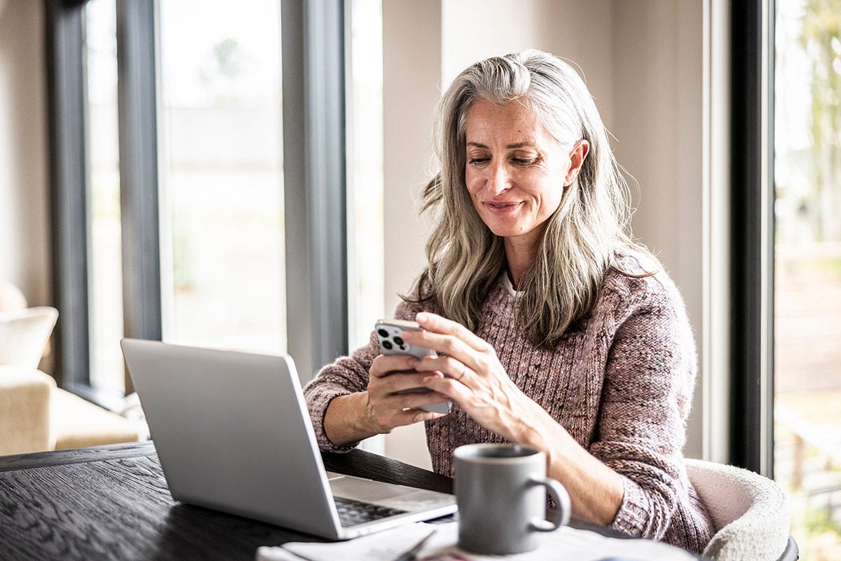 Senior woman using smartphone and laptop at home