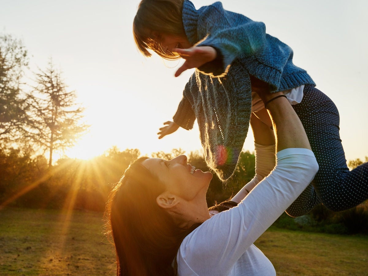 Mother lifting her child into the air at sunset.