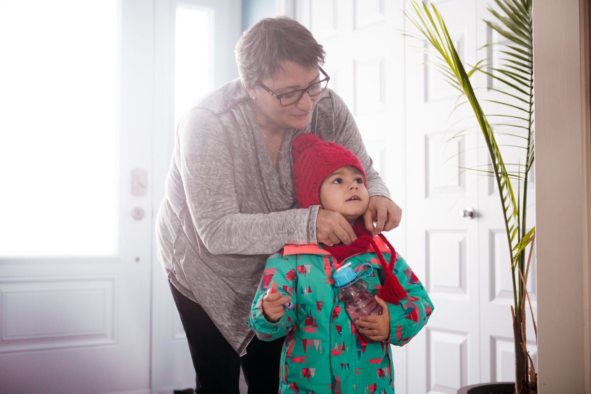 A person helps a child bundle up in winter clothing near the front door, adjusting the child’s hat before heading outside.