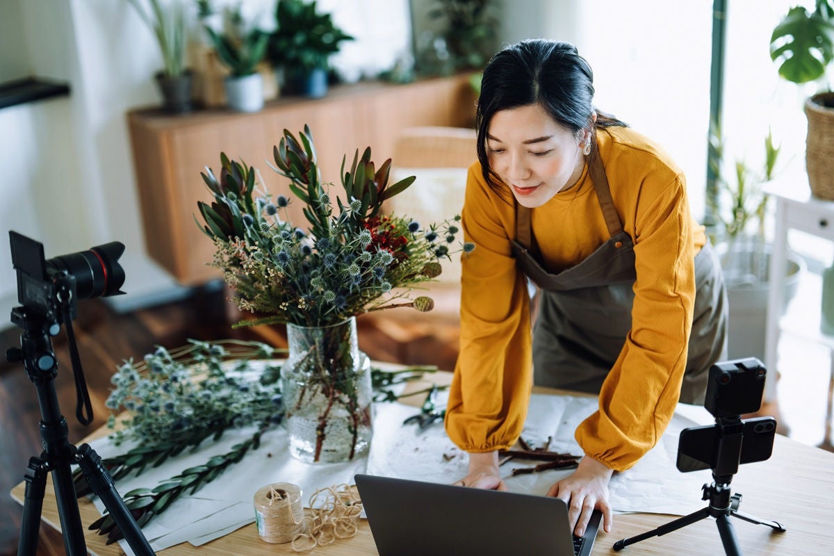 Florist preparing an arrangement while managing her small business on a laptop.