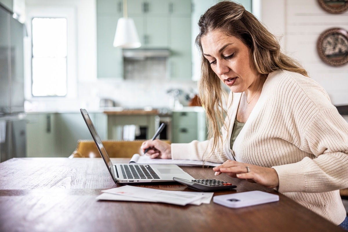 Woman paying bills with laptop at kitchen table