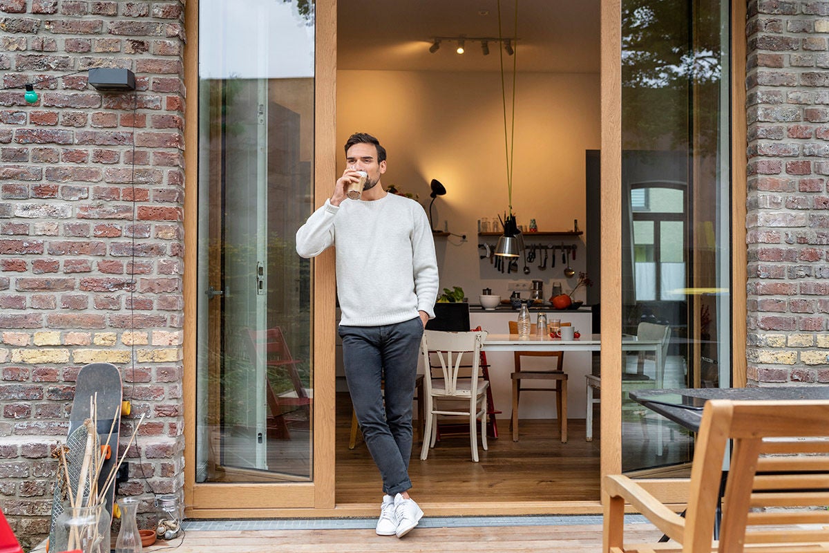 Man drinking a coffee while standing at the entrance of his patio