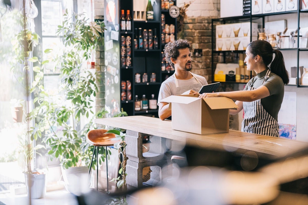 Small business owner and employee unpacking a delivery box inside a local shop.