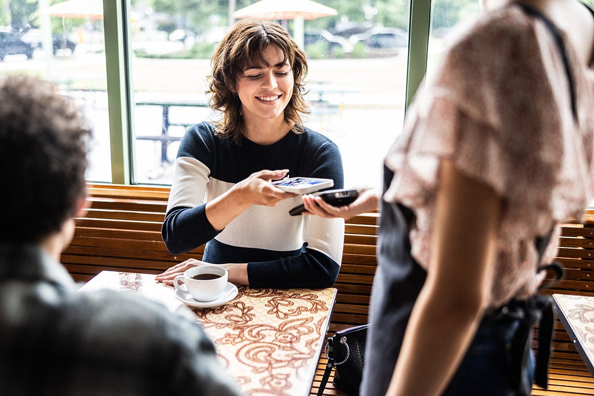Young woman paying her bill with a smartphone in coffeeshop
