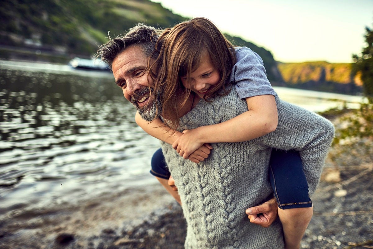 Dad giving a child a piggyback ride along a scenic riverside trail.