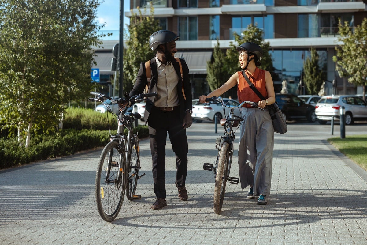 A joyful moment of two friends walking their bicycles along a city pathway, sharing laughter and enjoying a sunny day.