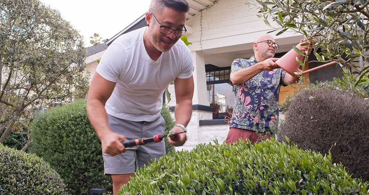 A mixed race gay couple gardening outside their house.