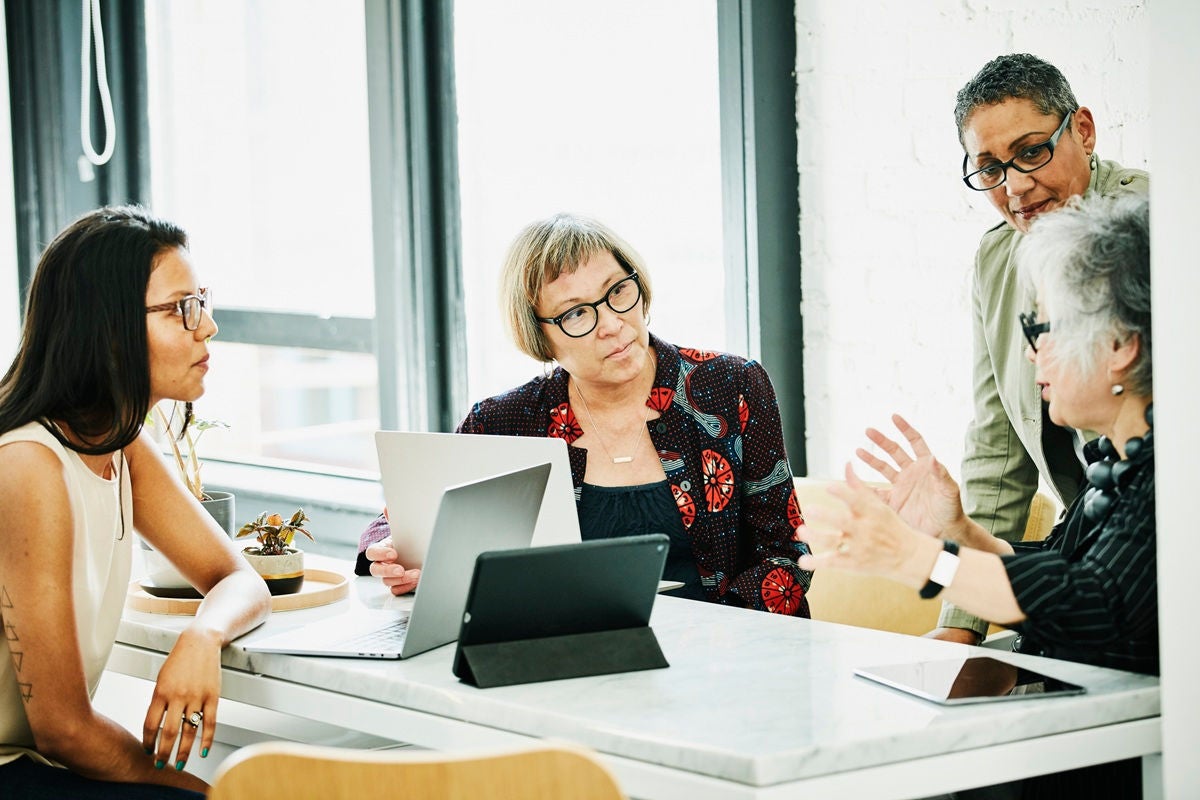 Group of financial advisors gathered around a table in a bright office space, discussing documents and working on laptops