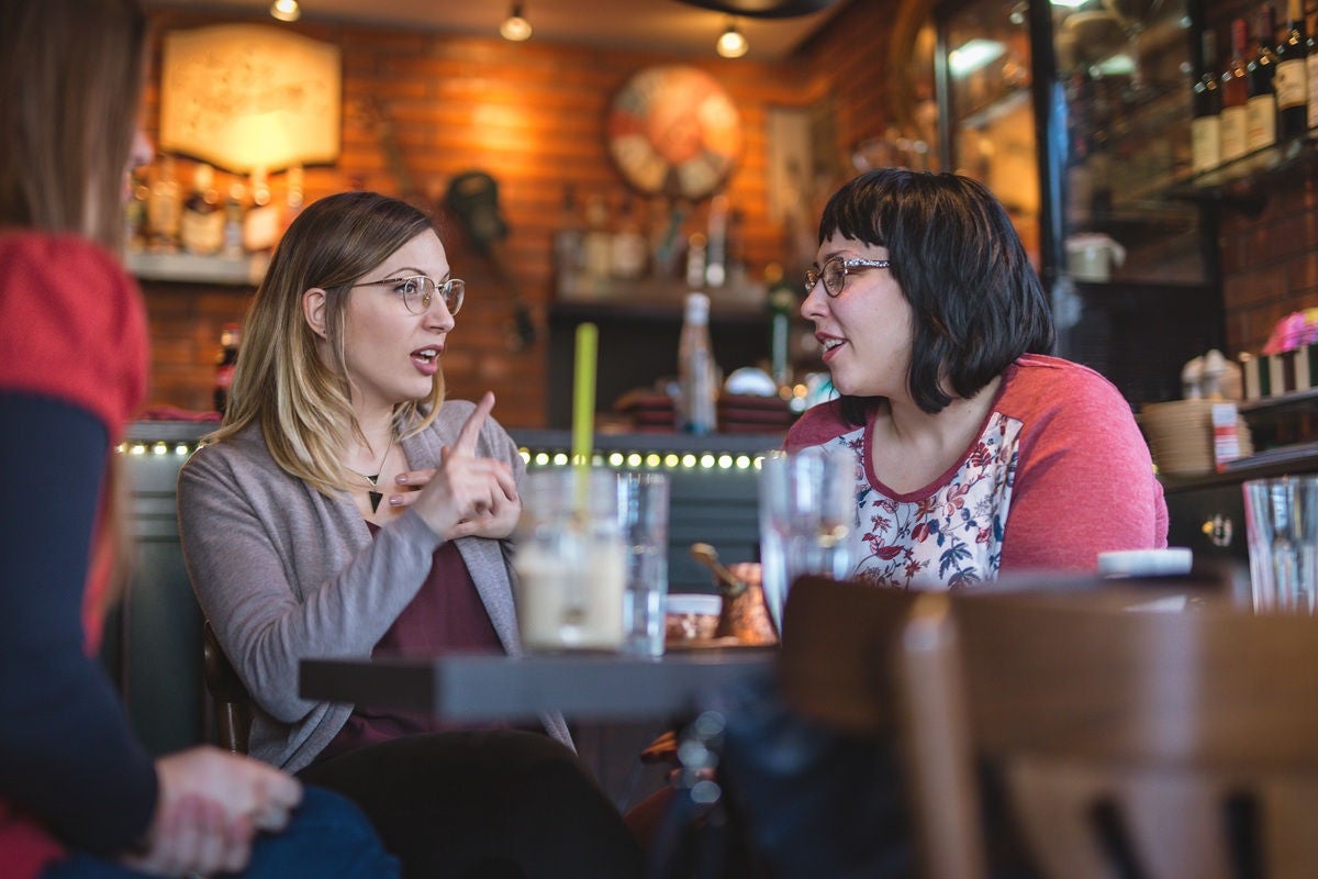 Two girls talkin in a busy cafe.