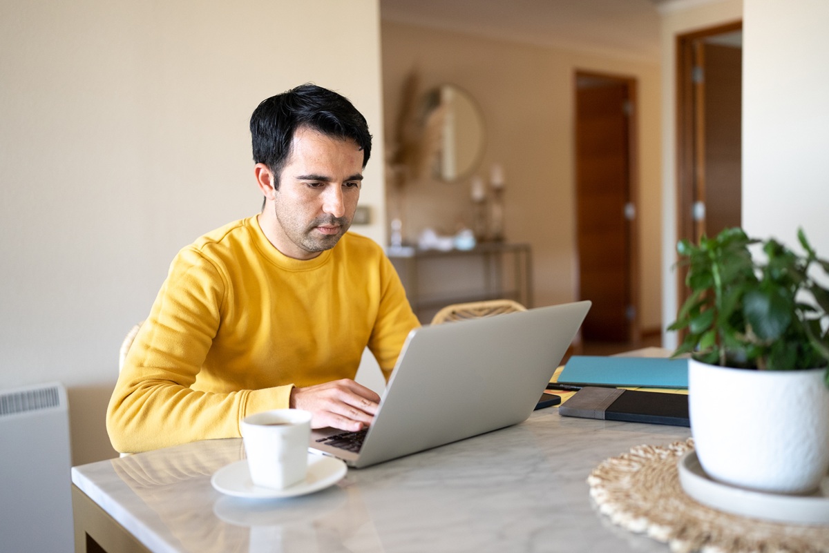 Individual working on a laptop at a home desk with coffee, representing remote work, online banking access, and managing personal finances from home.