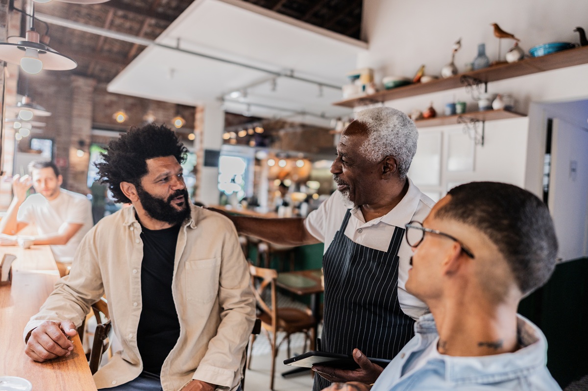 Server taking an order from two customers seated at a café counter.