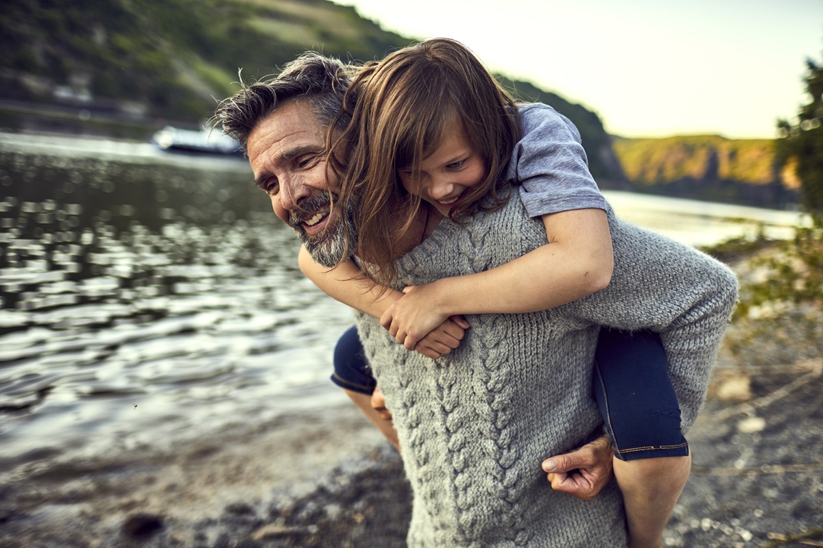 Dad giving a child a piggyback ride along a scenic riverside trail.