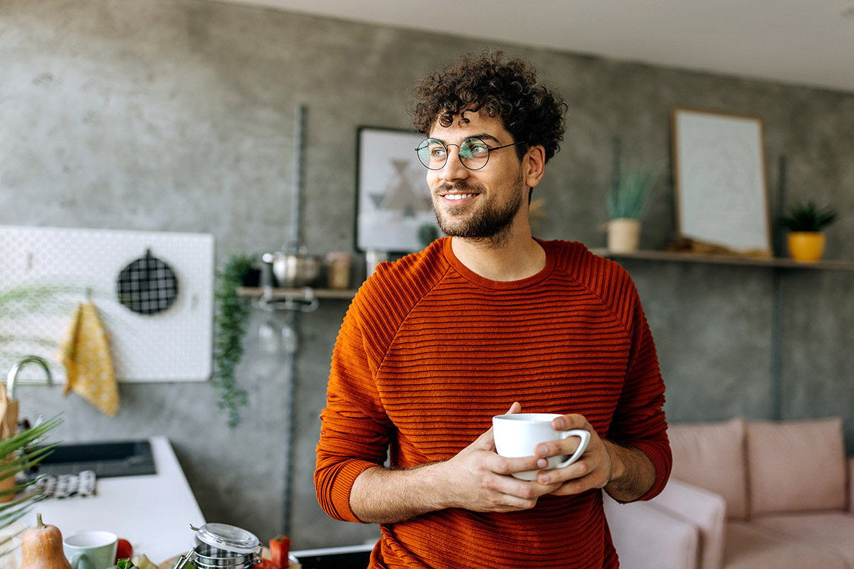 Individual standing in a modern home holding a coffee mug, representing a relaxed lifestyle supported by smart personal banking and everyday financial management.