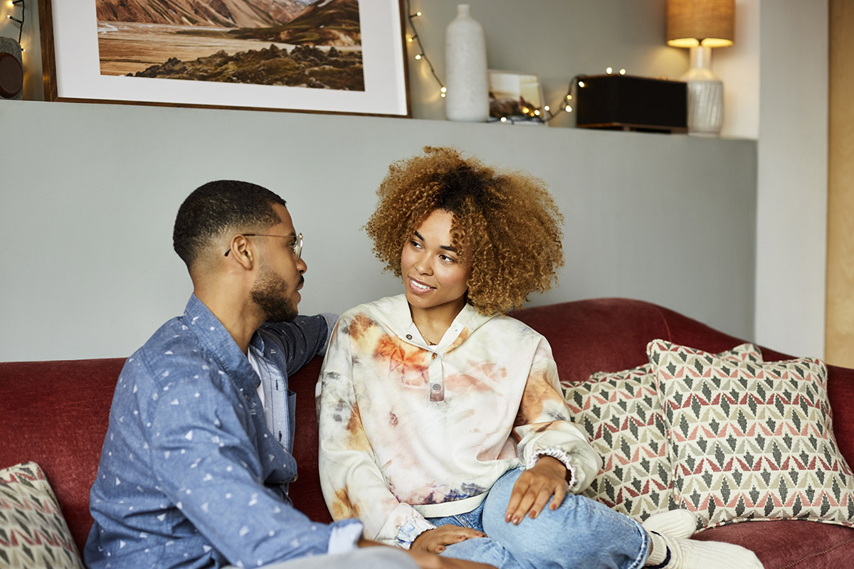 Young couple sitting in a sofa in a well lit home talking about financial wellbeing and future plans.