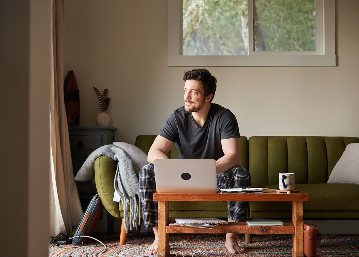 A person sits on a sofa, working on a laptop at a coffee table in a softly lit living room.