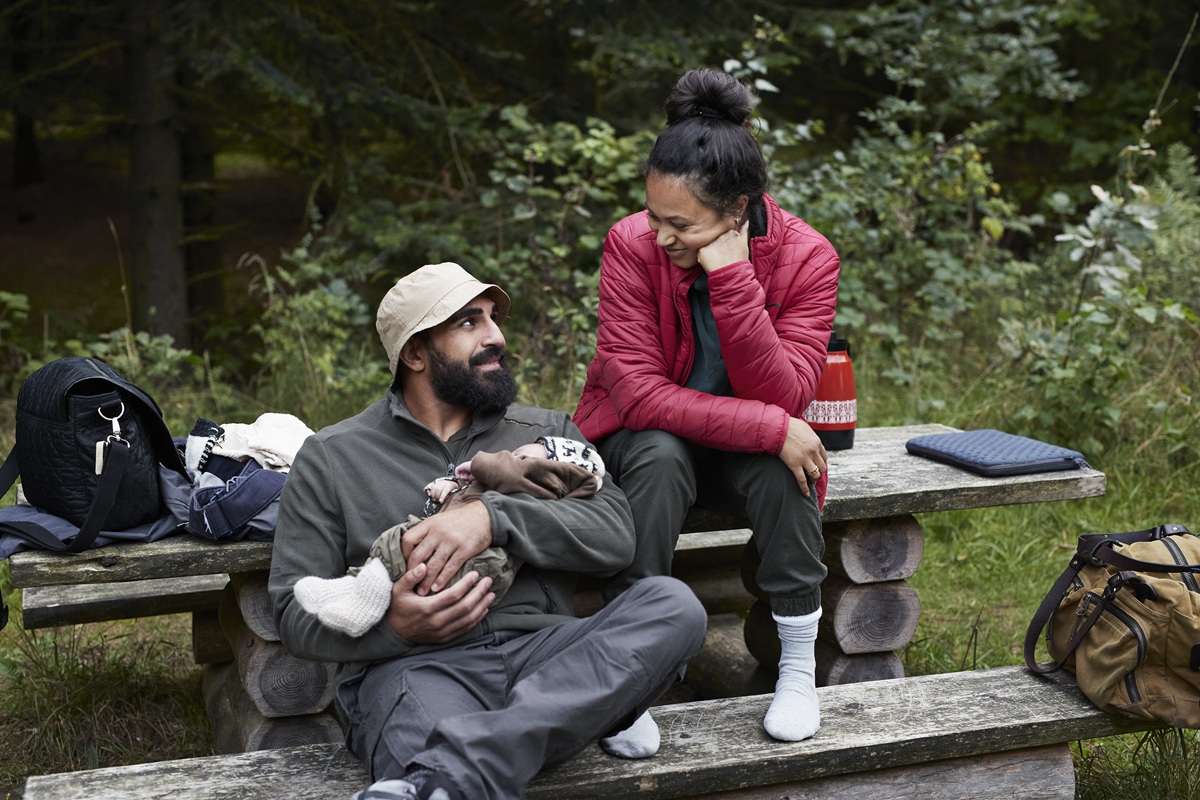 Parents resting on forest bench while holding baby during hike