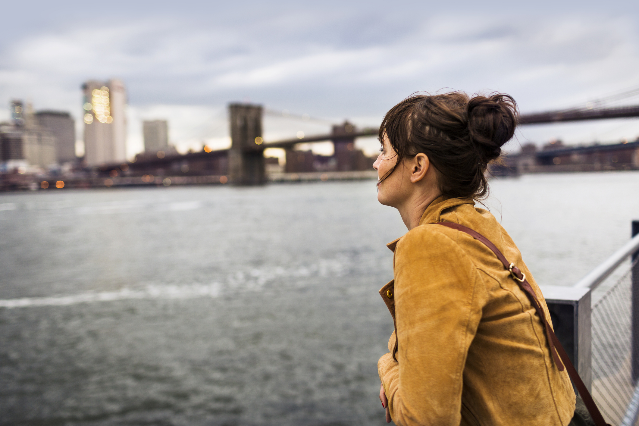 Woman looking over waterfront with bridge and city skyline in background.