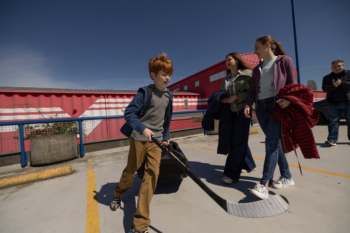 Child playing with hockey stick outdoors with family nearby.
