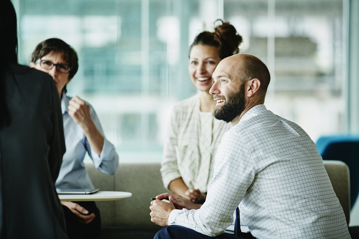 Small group of colleagues seated in a modern office, engaged in a discussion around a low table.