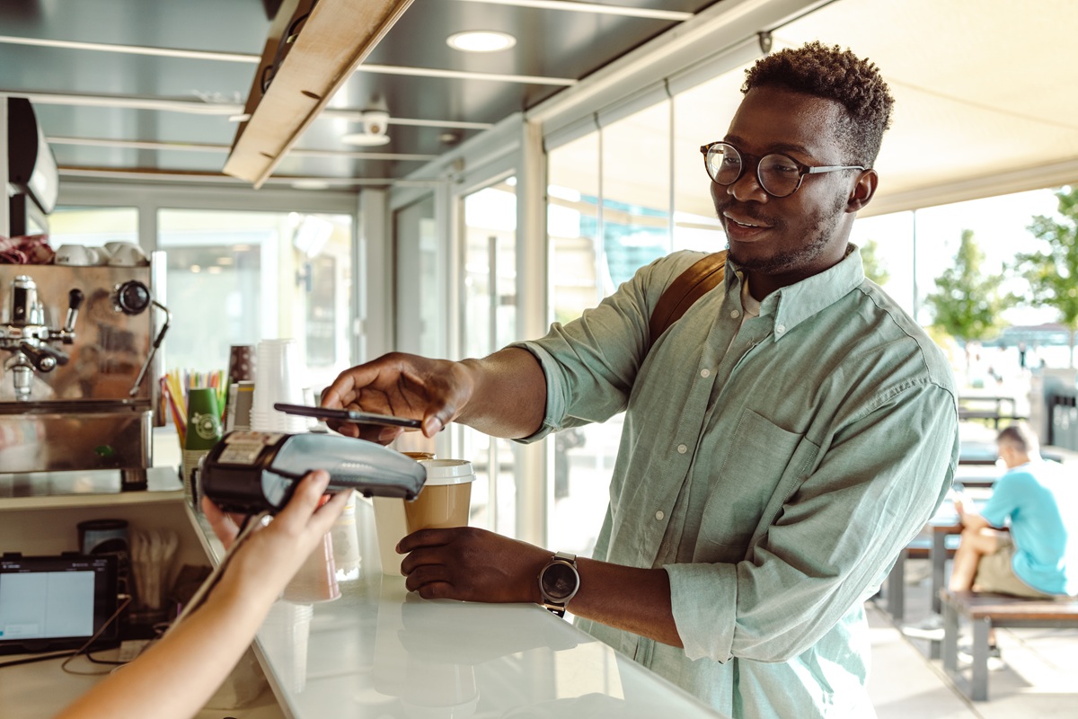 Young man paying at a café counter using a mobile card tap.