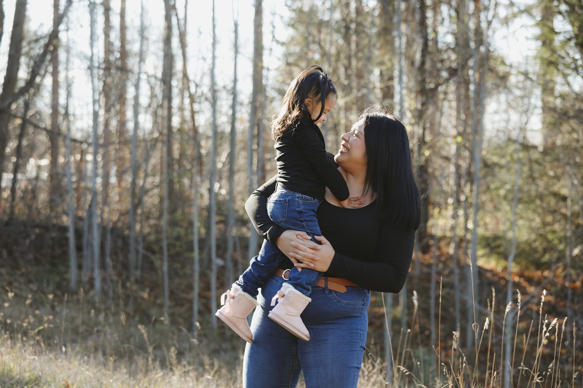 Parent holding a young child during a walk in a sunlit forest.