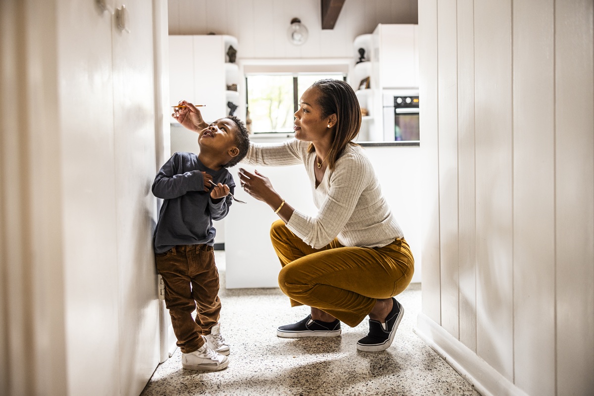 Parent measuring a child’s height in a bright home hallway.